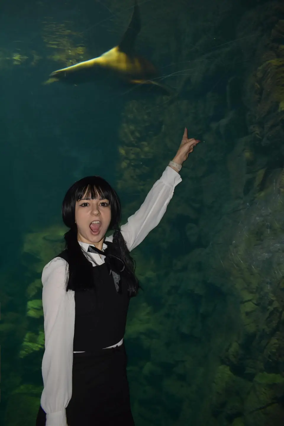 Moni in a black wig and dark uniform in front of an aquarium tank